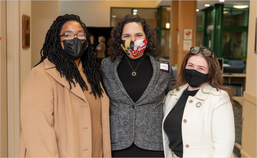 Three ladies arms wrapped around each other smiling looking at the camera with nose and mouth mask coverings