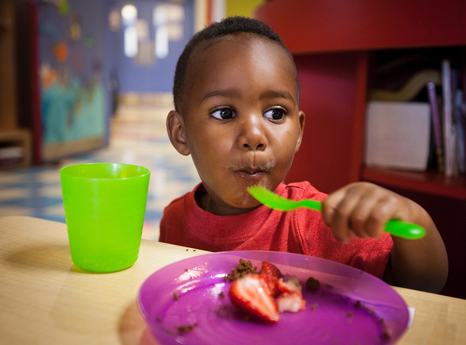 A child enjoys a mouthful of fruit with an excited look on his face.